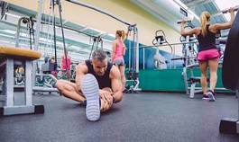 Fototapeta man stretching and women doing dumbbells exercises in gym