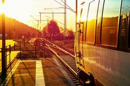 Plakat modern passenger train standing at countryside platform with beautiful landscape at sunset.