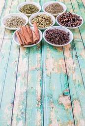 Plakat cardamom, star anise, cinnamon, clove, coriander seed spices and parsley, thyme, rosemary herbs in white bowls
