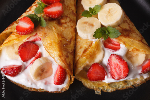 Fototapeta crepes with strawberries, bananas and cream close-up. horizontal