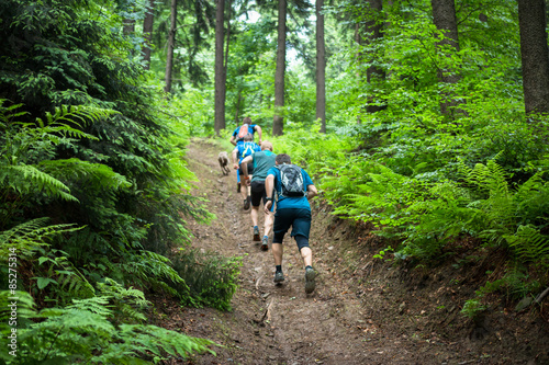 Naklejka four men running hard up the hill in the forest with fern