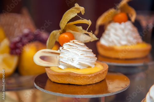Fototapeta Cakes with meringue and berries of cape gooseberry on a show-window of shop