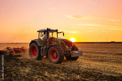 Obraz na płótnie Tractor on the barley field by sunset.